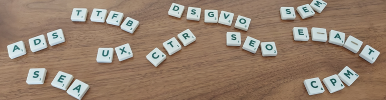 Verschiedene Abkürzungen aus dem Online-Marketing aus Scrabble-Buchstaben auf einem Holztisch.